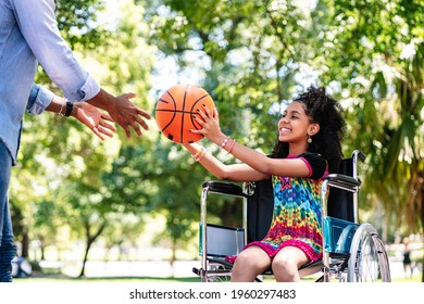 Little Girl In A Wheelchair Playing Basketball With Her Father.