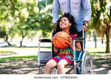 Little Girl In A Wheelchair Playing Basketball With Her Father.