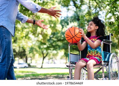 Little Girl In A Wheelchair Playing Basketball With Her Father.