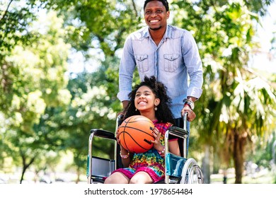 Little Girl In A Wheelchair Playing Basketball With Her Father.