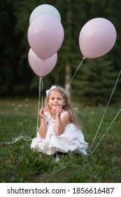 Little girl in white dress with balloons sitting on grass in park