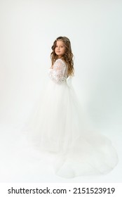 A little girl in a white dress and tiara posing on a white background in the studio. Portrait of child