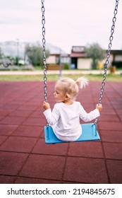 Little Girl In A White Tracksuit Rides On A Chain Swing