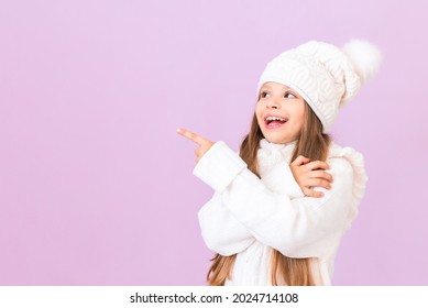 A little girl in a winter sweater and hat points to your ad on an isolated pink background.