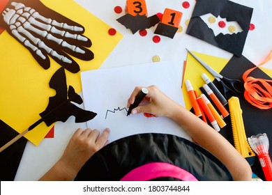 Little Girl In A Witch Costume Draw A Bat, For The Holiday Of Halloween On A Light Table. Halloween Decor. Handicraft. The Concept For Halloween. DIY.