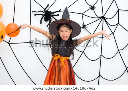 Little girl in the witch costume is holding Jack o’ lantern (pumpkin) standing extend arms with happiness. Asian cute child are smiling cheerfully in front of the backdrop decorated with spiderwebs. Foto stock © 