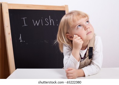 Little girl writes her wish list on a blackboard