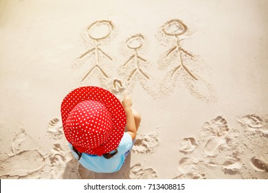 Little girl writing family into the sand.