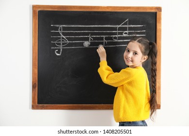 Little Girl Writing Music Notes On Blackboard In Classroom