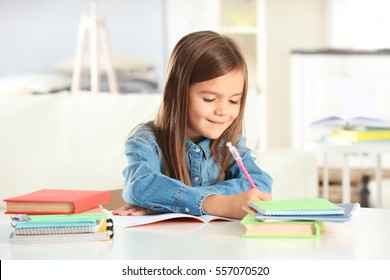 Little girl writing something in copybook and sitting at table