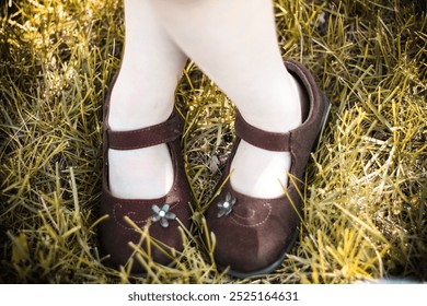 A little girl's crossed feet in Mary Jane style brown shoes, standing in the grass. - Powered by Shutterstock