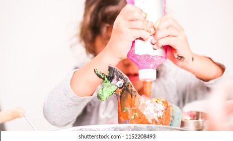 Little Girls Decorating Paper Mache Unicorn With Glitter And Paper Flowers.