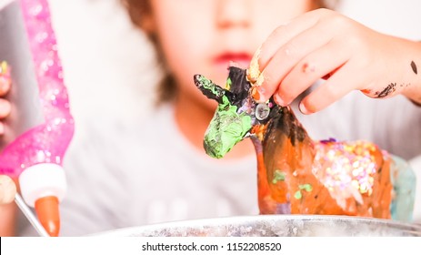 Little Girls Decorating Paper Mache Unicorn With Glitter And Paper Flowers.