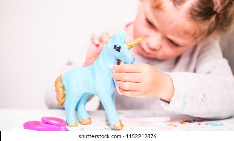 Little Girls Decorating Paper Mache Unicorn With Glitter And Paper Flowers.