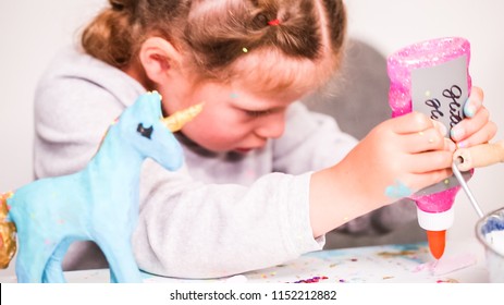 Little Girls Decorating Paper Mache Unicorn With Glitter And Paper Flowers.