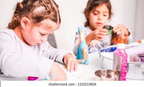 Little Girls Decorating Paper Mache Unicorn With Glitter And Paper Flowers.