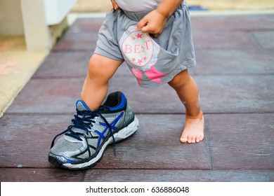 The little girl's feet try to put on her father's shoes with sandy hand and legs - Powered by Shutterstock