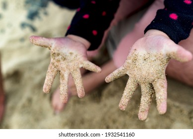 A little girl's hands as she digs for sand on the beach. She's wearing a winter top.