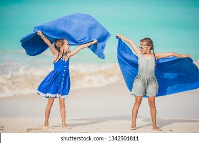 Little Girls Having Fun Running With Towel And Enjoying Vacation On Tropical Beach With White Sand And Turquoise Ocean Water