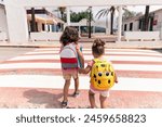 little girls holding hands, crossing a crosswalk to go to school.