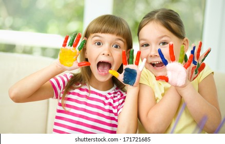 Kleine Mädchen malen mit Gouache und zeigen ihre malerischen Hände, während sie am Tisch sitzen