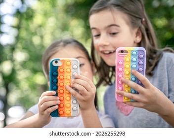 Little girls with phones in a case with pimples pop it, a trendy anti stress toy.
