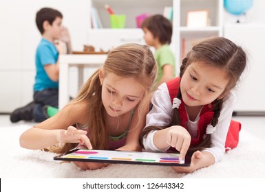 Little girls playing on a tablet computing device - laying on the floor - Powered by Shutterstock