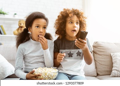 Little Girls Watching Discovery Channel And Eating Popcorn, Sitting On Sofa At Home