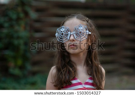Little girls wearing glasses. Halloween concept.A girl of 9-10 years old wore glasses with a spider design for Halloween or a summer theme party. A girl in a swimsuit on vacation.