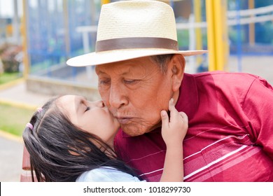 Little granddaughter giving a kiss to her grandfather wearing hat.
