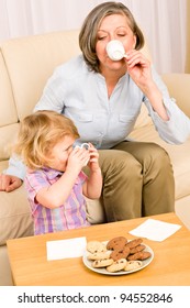 Little Granddaughter With Grandmother Eat Cookies Drink Tea Cup Together