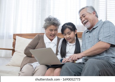 Little Granddaughter Teach Senior Elder To Surf Internet Using Computer And Technology Modern Lifestyle.Happy Asian Grandparent With Little Young Cute Grandchild Sitting On Sofa Playing Laptop.