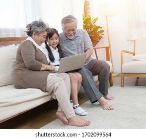 Little Granddaughter Teach Senior Elder To Surf Internet Using Computer And Technology And Modern Lifestyle.Happy Asian Grandparent With Cute Grandchild Sitting On Sofa Playing Laptop Together At Home