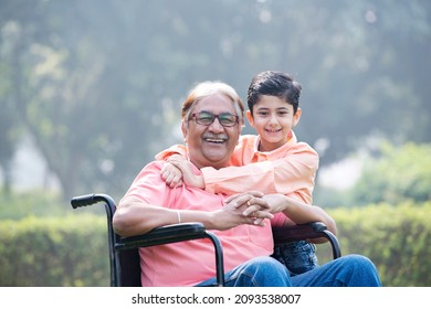 Little grandson pushing disabled grandfather on wheelchair at park
