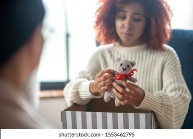 Little grey toy. Close up of curly woman holding little grey toy while telling about child loss