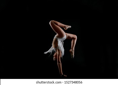 Little gymnast in a white sparkling dress on a black background doing a handstand - Shutterstock ID 1527348056
