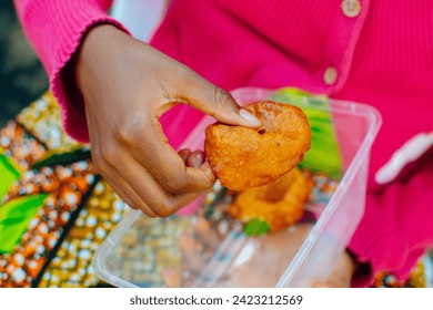 Little hand of an African Nigerian girl child, picking fried puff snacks from a transparent plastic plate to her mouth and eating at an event in Nigeria.