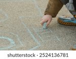 Little hand, drawing on the sidewalk with a blue colored chalk. Making art. Outside fun. Childhood memories 