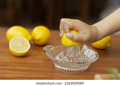 Little hand squeeze lemon juice with a lemon juicer glass on the wood table in the kitchen. Child prepare vegetable for a healthy cooking food vegetable concept. - Powered by Shutterstock