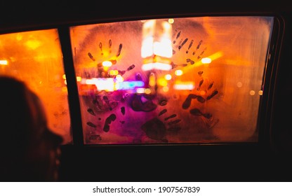 Little Kid’s Handprint On Wet Car Window Covered With Condensation In Night. Child’s Fingerprints On Glass Against Lights In Darkness.