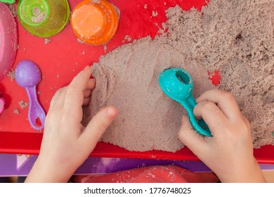 Little Hands Playing With Kinetic Sand And Molds On The Red Tray
