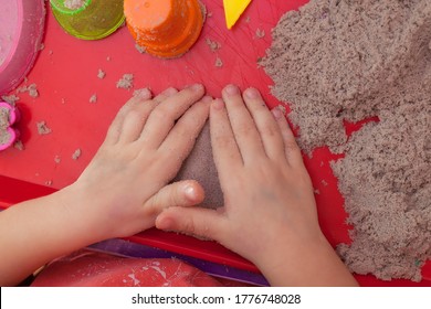 Little Hands Playing With Kinetic Sand And Molds On The Red Tray
