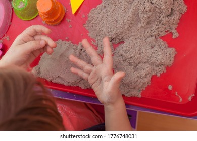 Little Hands Playing With Kinetic Sand And Molds On The Red Tray
