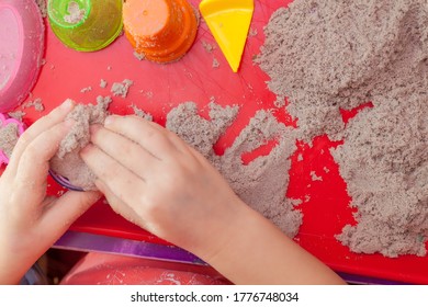 Little Hands Playing With Kinetic Sand And Molds On The Red Tray
