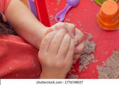 Little Hands Playing With Kinetic Sand And Molds On The Red Tray
