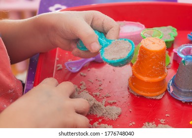 Little Hands Playing With Kinetic Sand And Molds On The Red Tray
