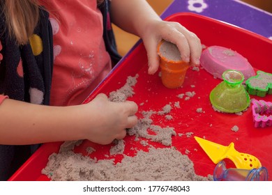 Little Hands Playing With Kinetic Sand And Molds On The Red Tray
