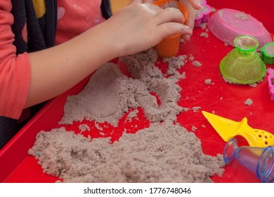 Little Hands Playing With Kinetic Sand And Molds On The Red Tray
