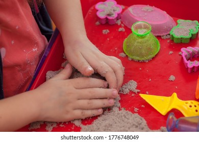 Little Hands Playing With Kinetic Sand And Molds On The Red Tray
