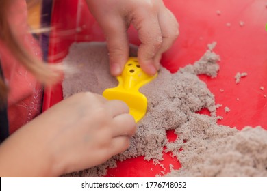 Little Hands Playing With Kinetic Sand And Molds On The Red Tray
